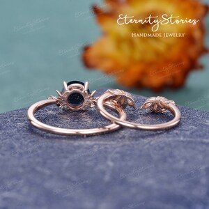 May include: A set of two rose gold rings with a black gemstone in the centre of the larger ring. The smaller ring has a leaf design. The rings are on a grey textured surface. Eternity Stories HANDMADE JEWELRY