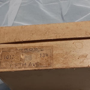 May include: A brown cardboard box with the text "ARROW" and "13 1/2" printed on it. The box also has the text "1012 FIFTH AVE" printed on it.