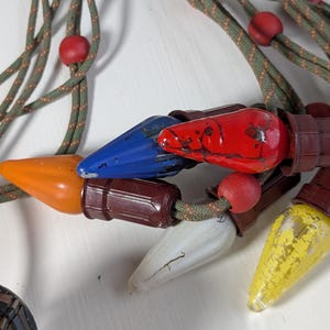 May include: A string of vintage-style decorative lights featuring multi-coloured bulbs in red, blue, orange, yellow, and white. The bulbs are attached to a green braided cord interspersed with small red wooden beads and brown plastic sockets.