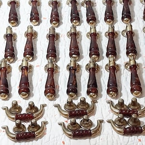 Könnte beinhalten: Eine Sammlung von 24 antiken Schrankbeschlägen. Die Griffe sind aus Holz mit einer dunkelbraunen Oberfläche und haben eine messingfarbene Metallbasis. Die Griffe sind in Reihen auf einer weißen Oberfläche angeordnet.