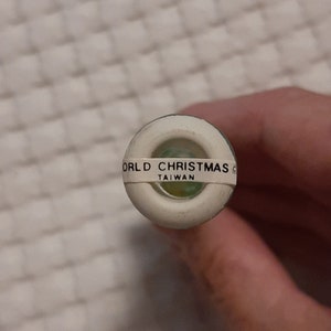 May include: Close-up of a white plastic bottle stopper with a green ring and the text "WORLD CHRISTMAS" and "TAIWAN" printed on it.