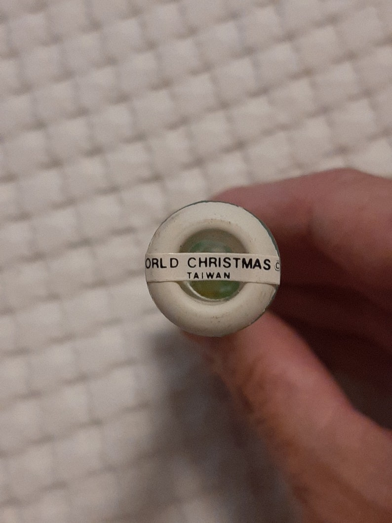 May include: Close-up of a white plastic bottle stopper with a green ring and the text "WORLD CHRISTMAS" and "TAIWAN" printed on it.