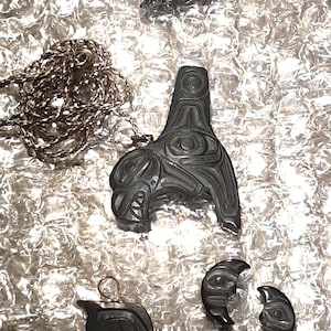May include: Four black carved wooden pendants with intricate designs. The pendants are in the shape of a bird, a face, and two crescent moons. The pendants are on a white background.