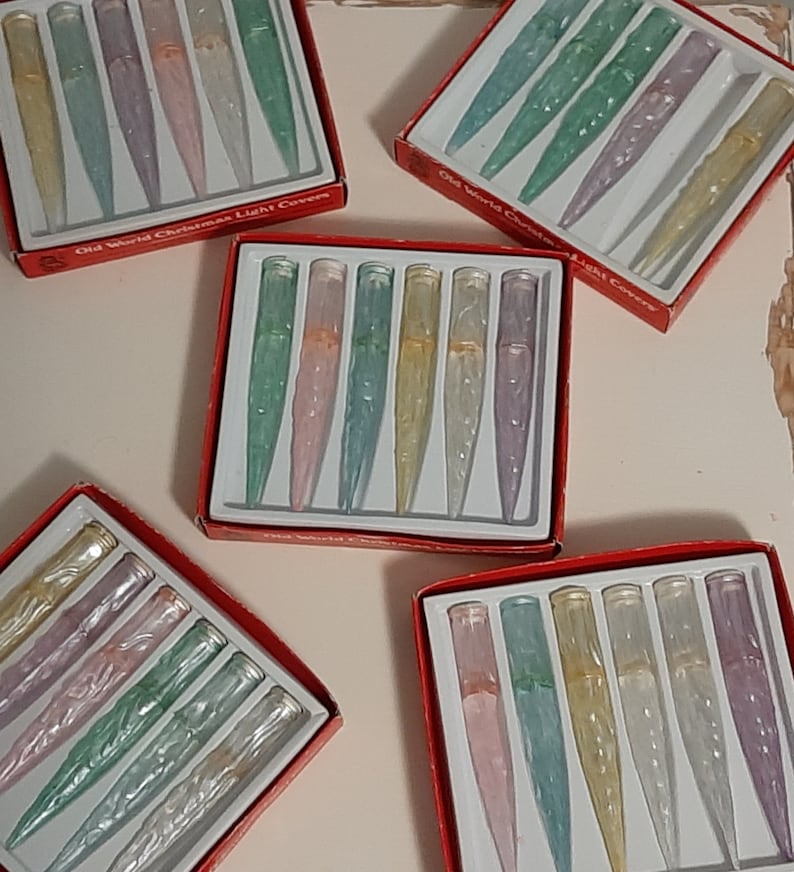 May include: Six boxes of Old World Christmas Light Covers. Each box contains six iridescent glass light covers in various colors, including pink, green, and blue. The boxes are red with white lettering.
