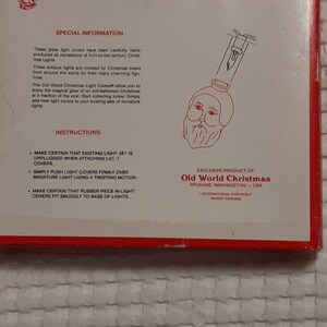 May include: A white box with red trim and the text "Old World Christmas Light Covers" printed on the front. The box features a black and white illustration of a Santa Claus light cover. The text "Exclusive Product of: Old World Christmas Spokane, Washington - USA" is printed on the bottom of the box.