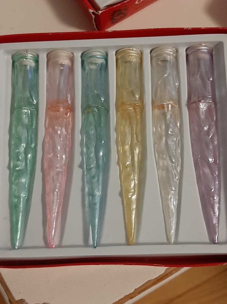 May include: Six iridescent glass bottle stoppers in a red and white box. The stoppers are in shades of green, pink, blue, yellow, white, and purple.