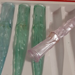 May include: Four glass icicles in a white tray. Three are green and one is pink.