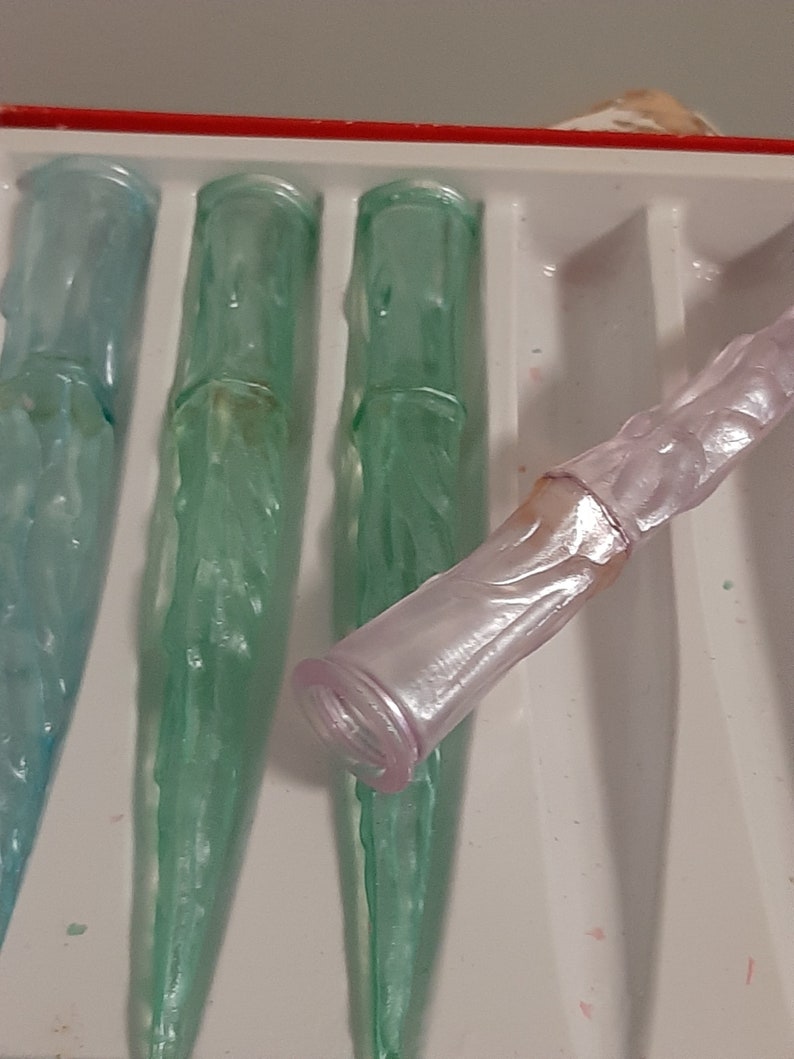 May include: Four glass icicles in a white tray. Three are green and one is pink.