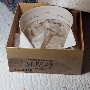 May include: A white collar in a brown cardboard box with a label that reads "Ferguson's 'Slip Easy' Calnagar Brand". The collar is in a box with tissue paper and has the text "Lion Collar & Shirts, Inc. 6045 Jordan 14 1/2" printed on it.