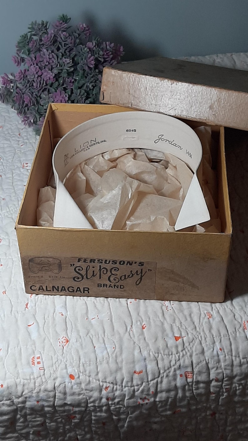 May include: A white collar in a brown cardboard box with a label that reads "Ferguson's 'Slip Easy' Calnagar Brand". The collar is in a box with tissue paper and has the text "Lion Collar & Shirts, Inc. 6045 Jordan 14 1/2" printed on it.