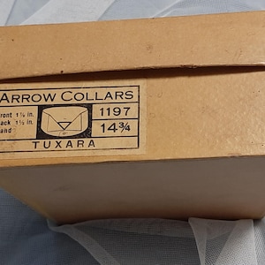 May include: A brown cardboard box with a white label that reads "ARROW COLLARS" and includes size information: "Front 1 1/8 in. Back 1 1/2 in. Band 14 3/4" and "TUXARA".