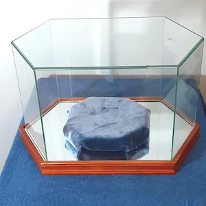 Könnte beinhalten: Sechseckige Glasvitrine mit Spiegelboden und Holzrahmen. Im Inneren befindet sich eine blaue Samtplattform. Die Vitrine ist für die Präsentation von Objekten konzipiert und bietet mehrere Blickwinkel.