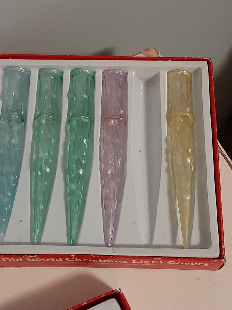 May include: A set of six vintage Christmas light covers in a red box. The covers are made of clear plastic and have a frosted, icicle-like design. The covers are in various colors, including blue, green, purple, and yellow.