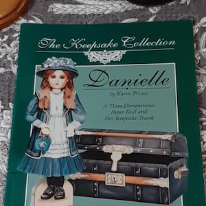 May include: A green book cover from "The Keepsake Collection" with a doll illustration and a trunk. The title reads "Danielle" by Karen Prince. The text states it is a three-dimensional paper doll and her keepsake trunk, based on an antique French bisque doll.