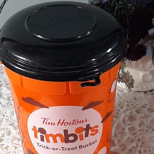 Puede incluir: Cubo naranja de Tim Hortons Timbits para pedir dulces, con asa y tapa negras. El cubo presenta gráficos temáticos de Halloween y el logotipo de Timbits. Un recipiente divertido para recolectar golosinas.