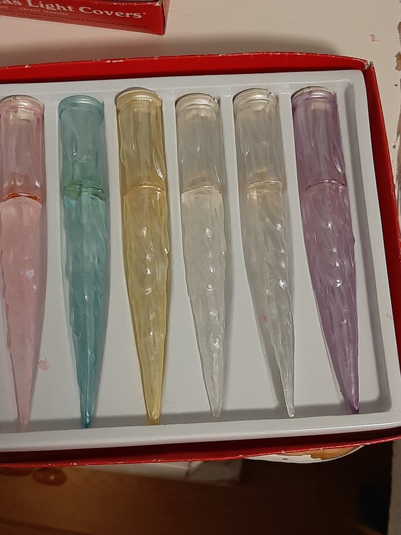 May include: A set of six icicle light covers in various colors, including pink, blue, yellow, white, and purple. The covers are packaged in a red box with the words "Light Covers" printed on the top.