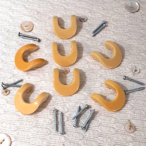 May include: A selection of light-yellow cabinet pulls and hooks, alongside screws and buttons, arranged on a textured surface. The pulls have a curved design, and the hooks are U-shaped. These items are suitable for furniture restoration or DIY projects.