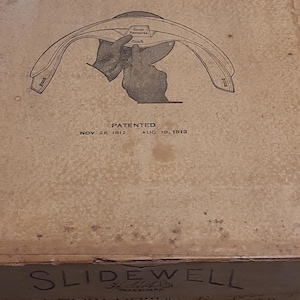 May include: A vintage box for a Slidewell brand hat. The box is brown with a black and white illustration of a hand adjusting a hat. The text on the box reads "Slidewell", "Patented Nov. 26, 1912 Aug. 19, 1913", and "14 1/2".