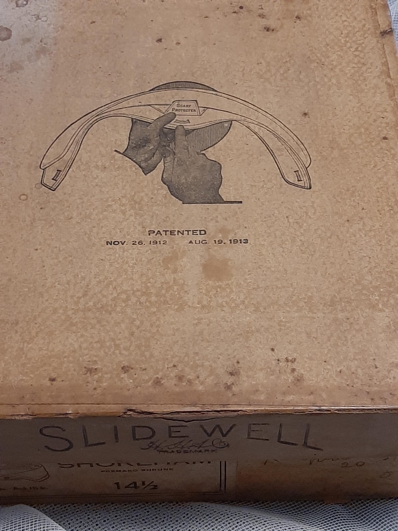 May include: A vintage box for a Slidewell brand hat. The box is brown with a black and white illustration of a hand adjusting a hat. The text on the box reads "Slidewell", "Patented Nov. 26, 1912 Aug. 19, 1913", and "14 1/2".