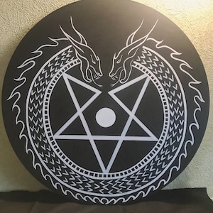 Puede incluir: Un diseño circular en blanco y negro con un pentagrama en el centro. Dos dragones blancos se miran, sus colas forman un círculo alrededor del pentagrama. El fondo es negro.