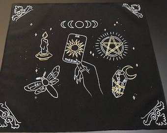 以下が含まれることがあります： 白い糸と金の糸で刺繍された黒い布。タロットカード、蛾、ろうそく、ペンタグラム、クリスタル、三日月が描かれている。カードには「XIX 太陽」と書かれている。