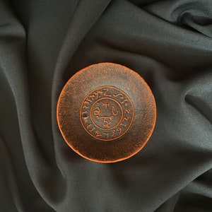 K&ouml;nnte beinhalten: Eine kleine, runde Schale aus terracotta in Terrakottafarbe mit einem erhabenen, kreisf&ouml;rmigen Design in der Mitte. Das Design zeigt ein Symbol mit einem Schl&uuml;ssel und anderen Markierungen, umgeben von Zahlen.