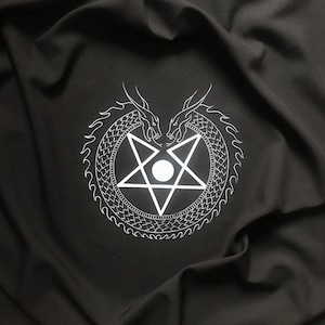 Pode incluir: Um pentagrama branco com um círculo no centro é cercado por dois dragões brancos que se enfrentam. O design está em um fundo de tecido preto.
