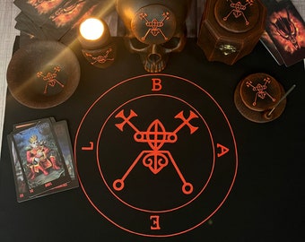 May include: A black cloth with a red sigil in the center. The sigil is surrounded by the letters B, A, E, and L. There is a skull, a candle, and a wooden box with a sigil on the top. There are also several cards with images of demons on them.