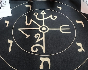 May include: A black cloth circle with a gold circle in the center. The gold circle has a symbol with a trident, a cross, and a circle in the center. The outer circle has Hebrew letters around it.