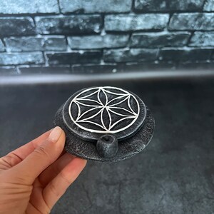 May include: A black and white ceramic incense burner with a flower of life design. The burner has a small hole in the center for incense sticks.
