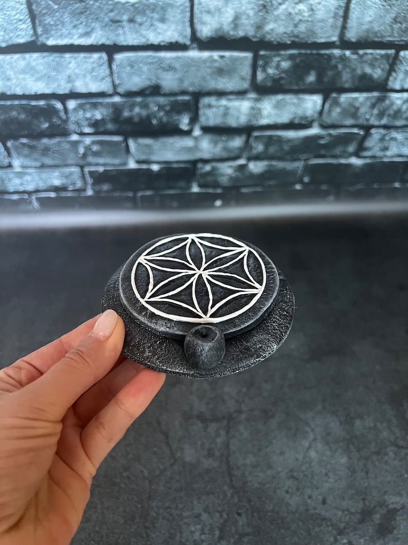 May include: A black and white ceramic incense burner with a flower of life design. The burner has a small hole in the center for incense sticks.
