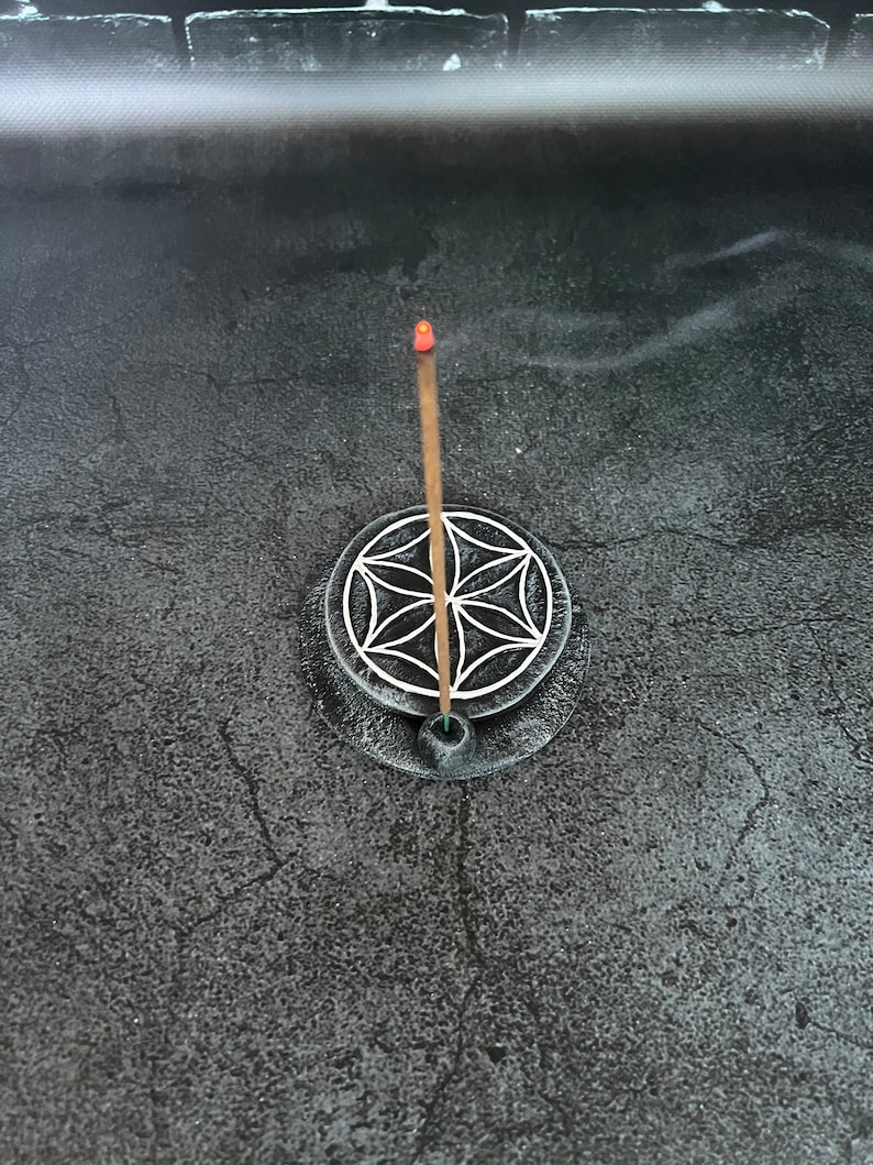 May include: A black incense holder with a white geometric design and a burning incense stick.