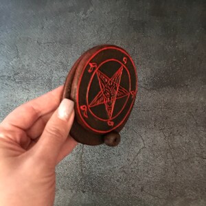 May include: A small, round, wooden box with a red pentagram design on the lid. The pentagram has a goat's head in the center.