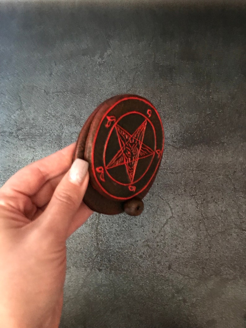May include: A small, round, wooden box with a red pentagram design on the lid. The pentagram has a goat's head in the center.