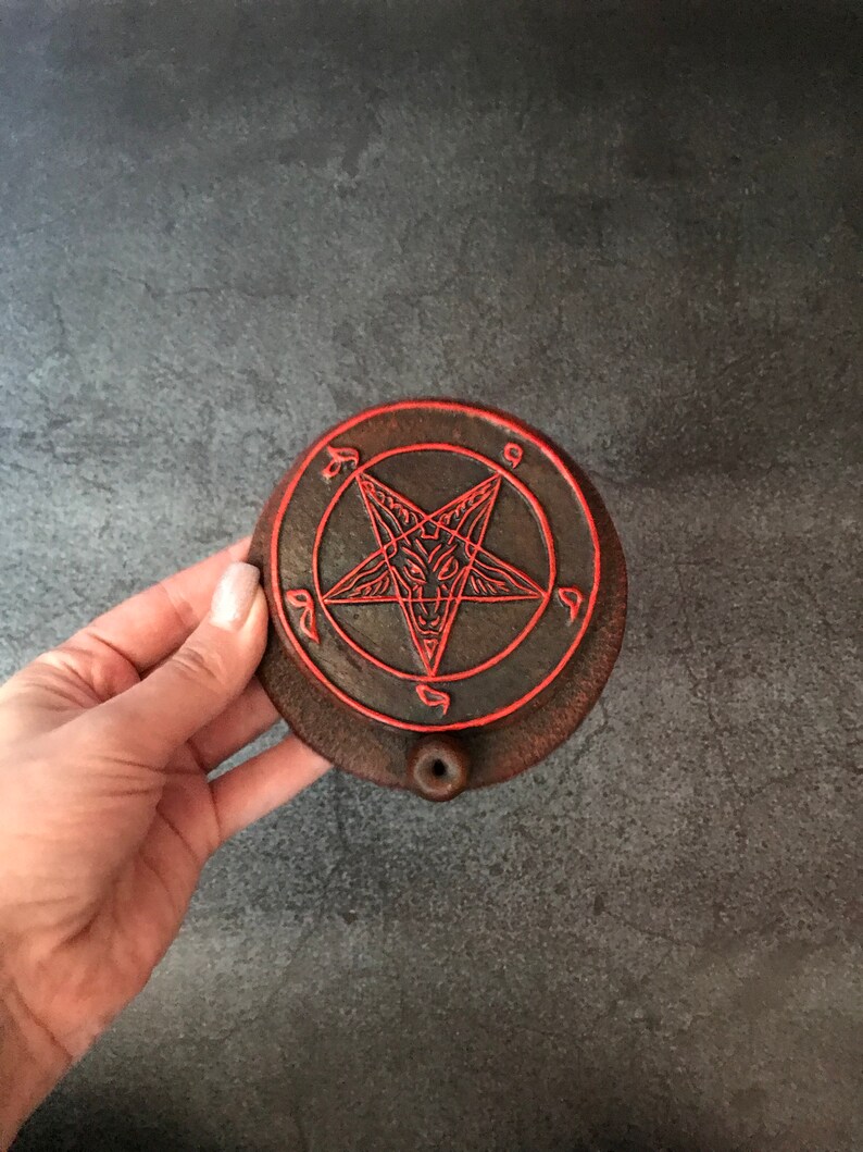May include: A dark brown ceramic incense burner with a red pentagram design. The burner has a small hole in the center for incense sticks.