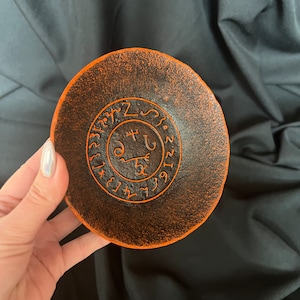 K&ouml;nnte beinhalten: Orangefarbene und schwarze Keramikschale mit einem kreisf&ouml;rmigen Design, das ein Symbol und Zahlen zeigt. Das Symbol ist von einem Kreis mit Zahlen umgeben.
