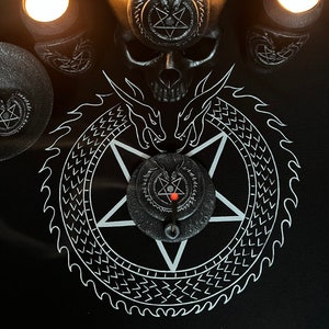 Puede incluir: Un pentagrama blanco y negro con un diseño de dragón alrededor del perímetro. Un cráneo negro con un pentagrama en la frente se sienta sobre el pentagrama. Tres candelabros negros con velas encendidas se colocan alrededor del pentagrama.