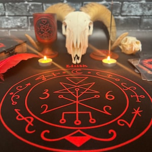 Puede incluir: Un mantel de altar negro con un diseño de pentagrama rojo, velas, un cráneo de carnero y un cáliz de madera. La palabra "Lilith" está impresa en la tela. Un tema místico y oculto.