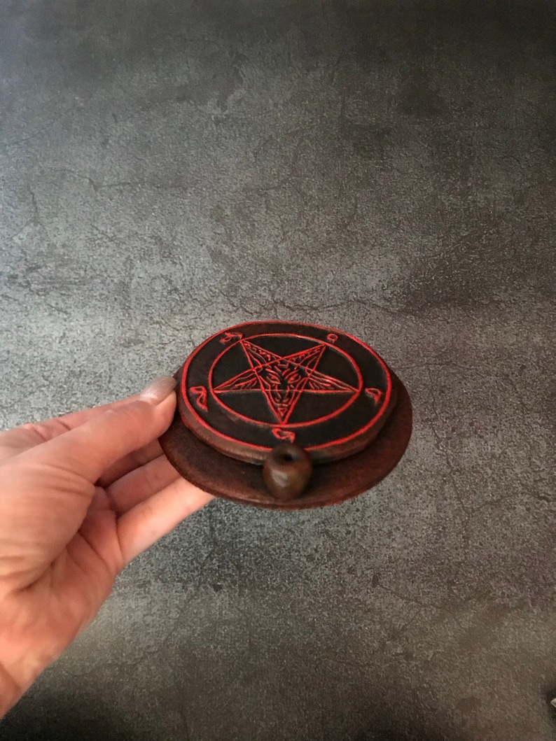 May include: A dark brown leather incense burner with a red pentagram design. The burner has a small hole in the center for incense sticks.