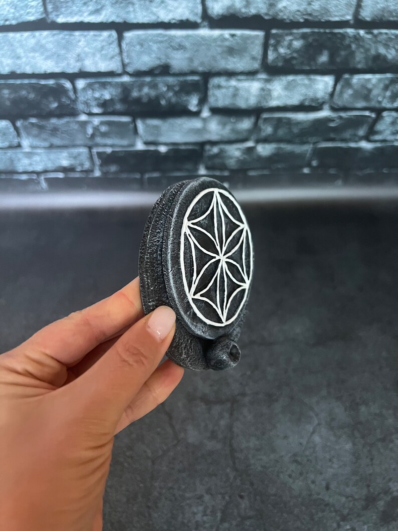 May include: A gray ceramic incense burner with a white geometric design. The burner has a small hole on the side for incense sticks.
