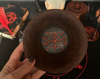 May include: A brown ceramic bowl with a red symbol inside. The symbol is a circle with a cross in the center and three crescent moons around it.