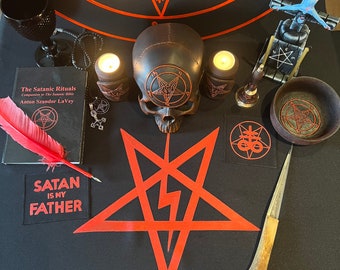 May include: A black altar cloth with a red pentagram, a skull with a pentagram on its forehead, two lit candles, a book titled "The Satanic Rituals", a feather, a bone, a small bell, a bowl, a sword, and a patch that reads "Satan is my Father".
