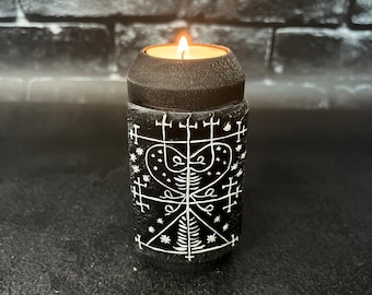 May include: A black candle holder with a white sigil design. The candle is lit and the flame is visible.