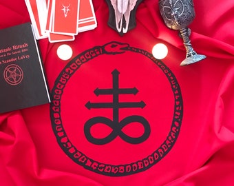 May include: A red cloth with a black sigil of the Leviathan, a symbol of Satanism. The sigil is surrounded by a circle of text. There are tarot cards, a book titled "Satanic Rituals", a skull, and a chalice with a pentagram on it.