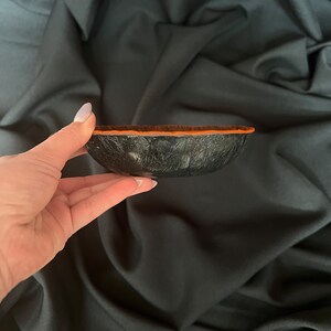 K&ouml;nnte beinhalten: Eine kleine schwarze Schale mit einer strukturierten Oberfl&auml;che und einem orangefarbenen Rand. Die Schale ist aus einem Material gefertigt, das Leder &auml;hnelt.