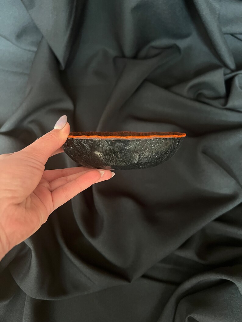 K&ouml;nnte beinhalten: Eine kleine schwarze Schale mit einer strukturierten Oberfl&auml;che und einem orangefarbenen Rand. Die Schale ist aus einem Material gefertigt, das Leder &auml;hnelt.