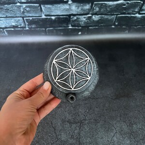 May include: A round, gray stone incense burner with a white geometric design. The burner has a small hole on the side for incense sticks.