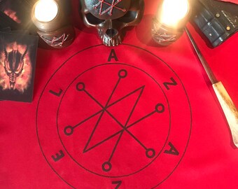 May include: A red cloth with a black circle containing a star with a pentagram inside. The circle has the letters "LAEZNA" around the outside. There are two lit candles and a skull with a pentagram on its forehead.
