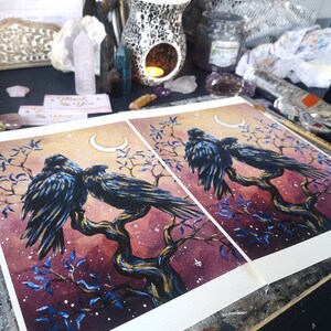 May include: Two black crows perched on a branch with a crescent moon in the background. The painting is done in watercolor and has a dark, mystical feel. The background is a deep purple with blue and gold accents.
