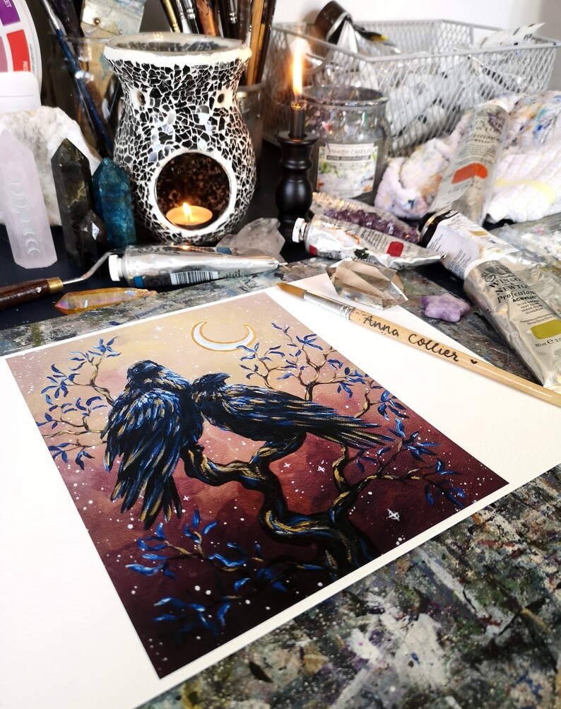 May include: A watercolor painting of two black ravens perched on a tree branch under a crescent moon. The background is a dark purple with gold and white accents. The painting is signed "Anna Collier".